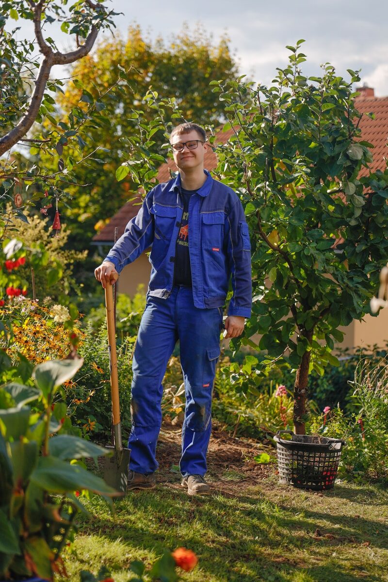 Man in blue work clothes holding shovel in garden